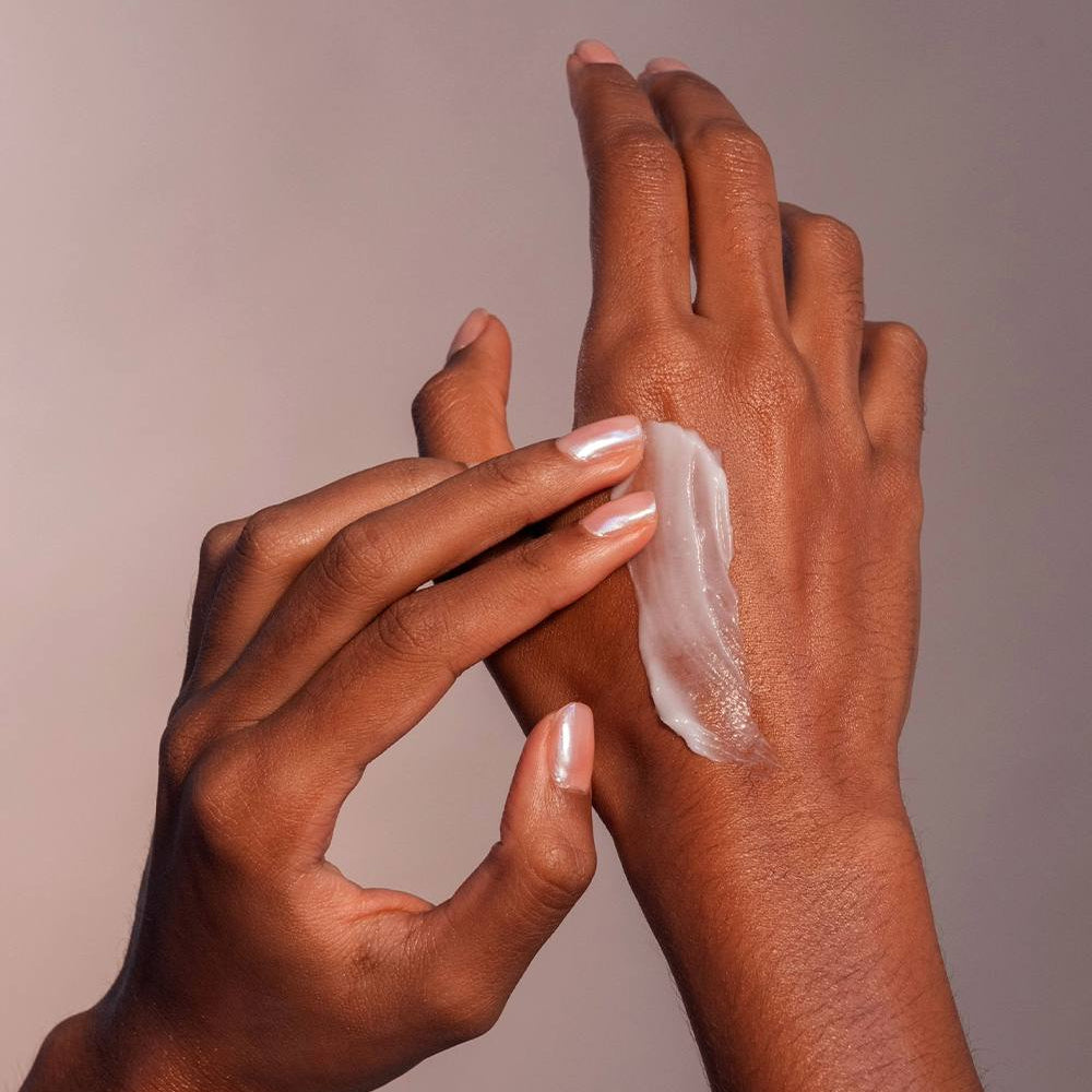 Two hands applying cream to a palm against a neutral background