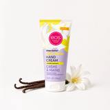 A squeeze tube of EOS Shea Better Hand Cream, vanilla creamer, standing upright on a white background with vanilla beans and a white flower prop.
