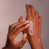 Two hands applying cream to a palm against a neutral background