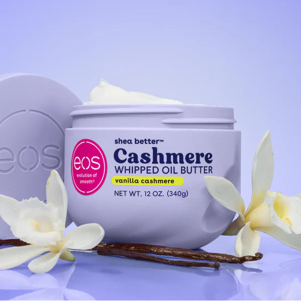 EOS Cashmere Whipped Oil Butter in a light lavender jar, styled with vanilla flowers and beans on a reflective lavender surface.